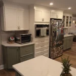 White kitchen with built-in refrigerator and dark green island cabinetry