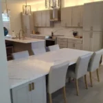 White kitchen with long marble island, wood dining table and upholstered chairs