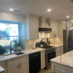 Two-tone white and dark green kitchen with marble counters and window over the sink
