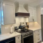 White kitchen with dark wood range hood and marble tile backsplash