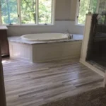 Soaking tub near window with wood look flooring
