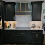Dark green kitchen with gold range hood and mosaic tile backsplash