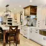 White kitchen with wood beam range hood, pendant lighting and dining table