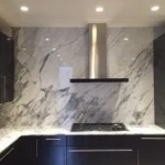 Dark kitchen with marble backsplash and stainless range hood