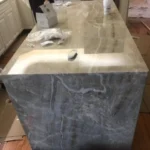 Close-up of gray marble waterfall island with farmhouse sink