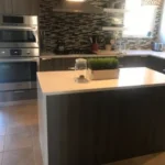 Dark kitchen with white waterfall island and mosaic backsplash