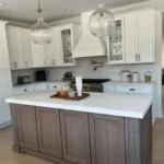 White kitchen with marble island, glass-front upper cabinets and pendant lights