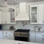 White kitchen with stainless range, glass-front cabinets and marble backsplash